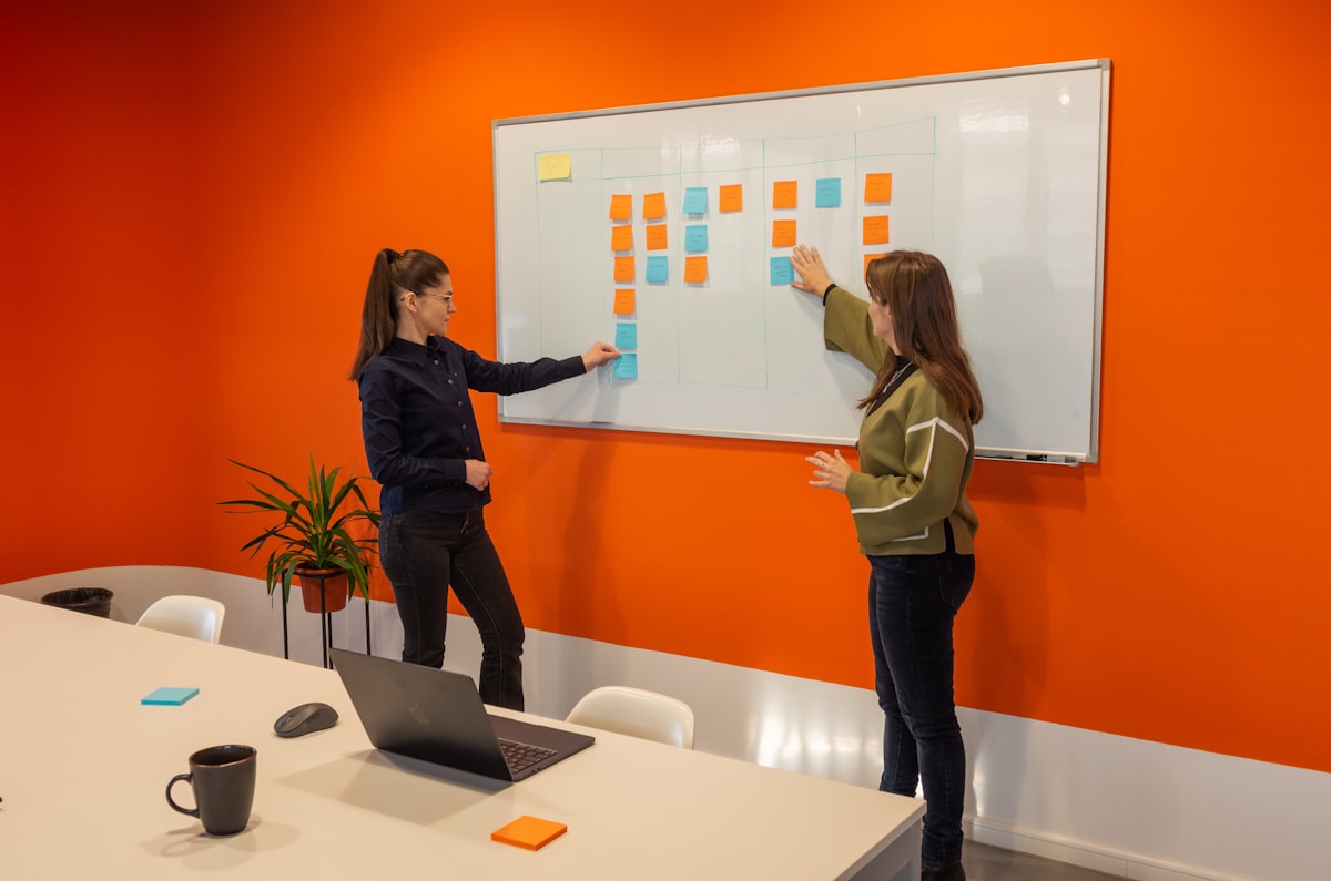 Two female coworkers collaborating with sticky notes on a whiteboard in a meeting room